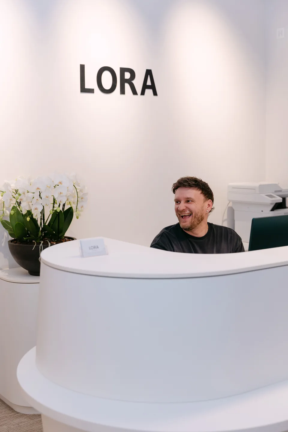 Empfang der Zahnarztpraxis LORA mit LORA-Schriftzug und einem lächelnden Mitarbeiter