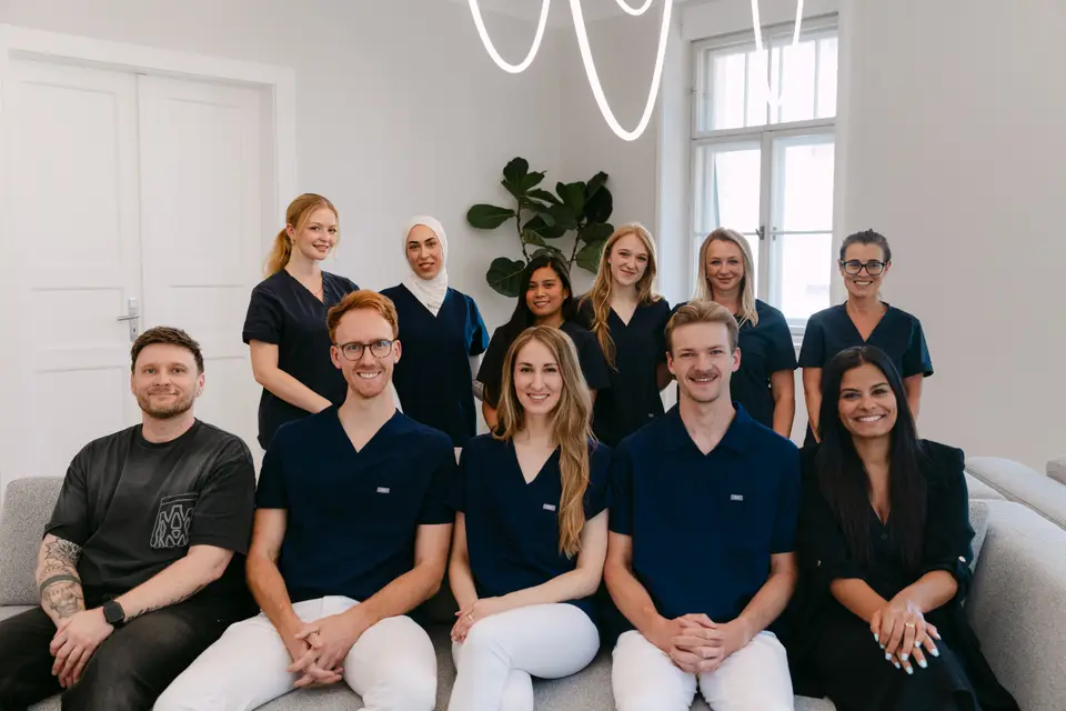 Das Team der Zahnarztpraxis LORA, elf Personen auf einem grauen Sofa in der Praxis