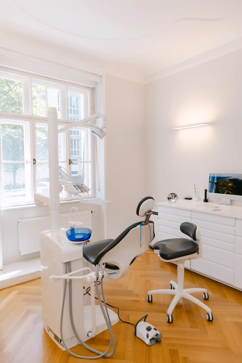 Behandlungszimmer mit Zahnarztstuhl, Behandlungsunit und einem Fenster zur Straße