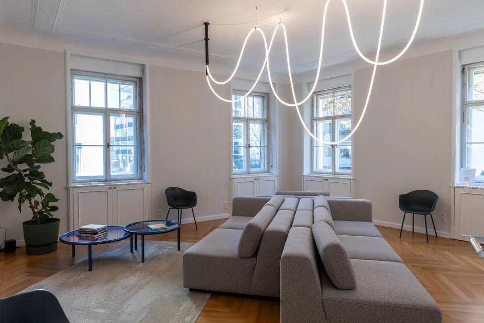 Wartezimmer der Zahnarztpraxis LORA Schwabing mit grauem Sofa und geschwungener Leuchte