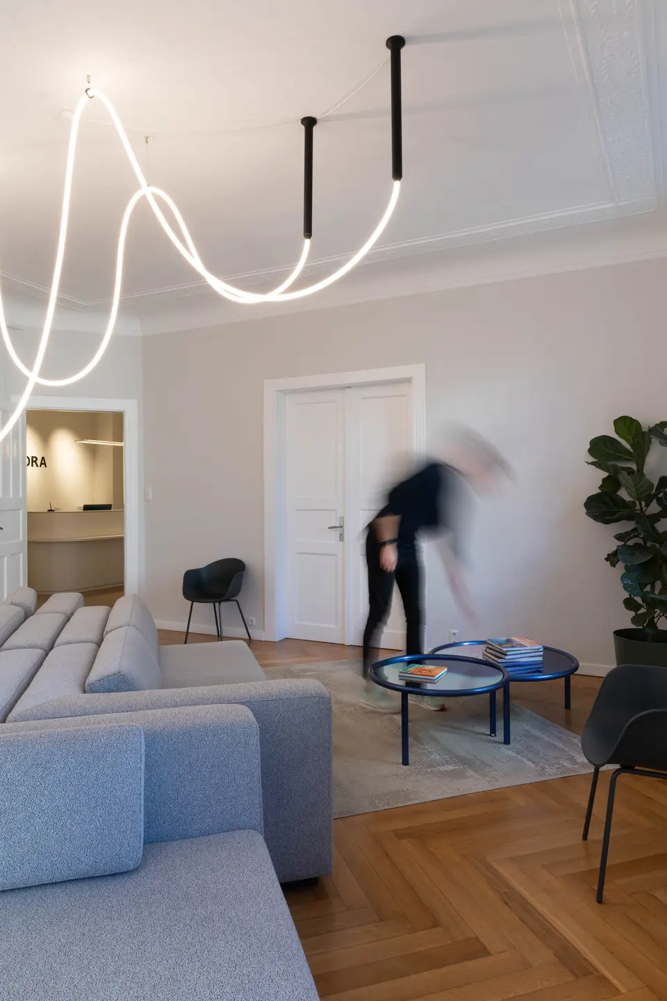 Wartebereich mit grauem Sofa, blauen Tischen und geschwungener Deckenleuchte